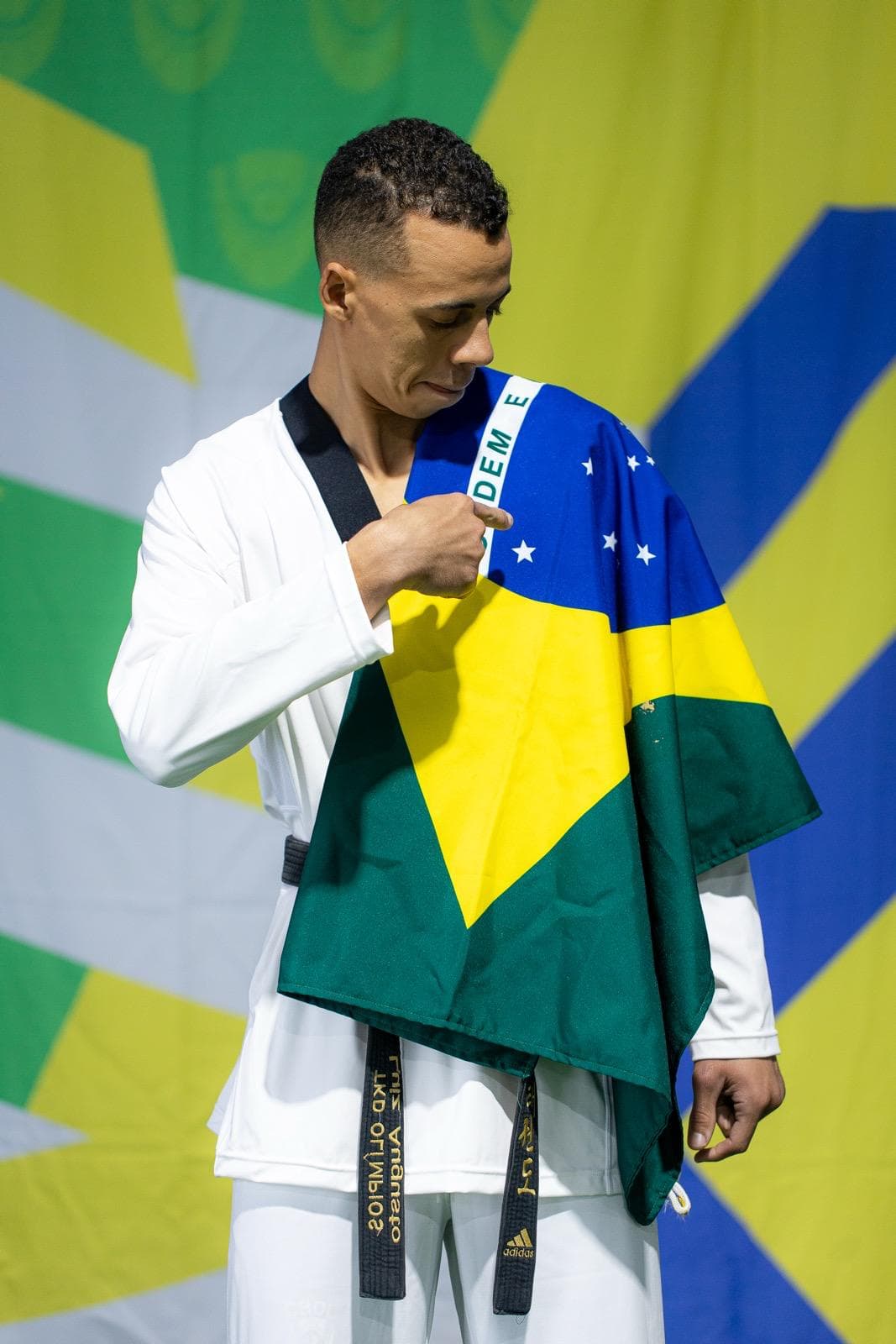 Luiz Augusto de dobok e faixa preta, com a bandeira do Brasil sobre o ombro